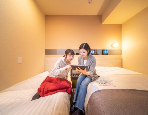 two women sitting on a bed looking at a tablet at Super Hotel Premier Akihabara in Tokyo