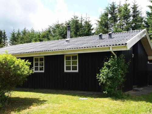 a black house with a tin roof on a yard at 6 person holiday home in Blokhus in Blokhus