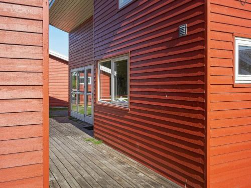 een rood huis met een houten vloer en een gebouw bij 6 person holiday home in Gudhjem in Gudhjem