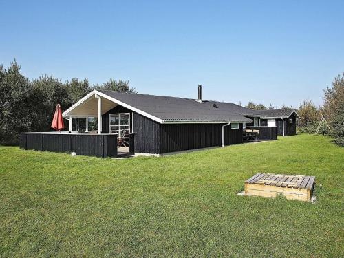 a black house with a yard with a grass field at 8 person holiday home in Hj rring in Lønstrup