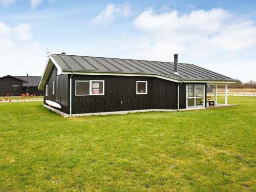 6 person holiday home in Hadsund في Øster Hurup: منزل أسود في حقل مع ساحة خضراء