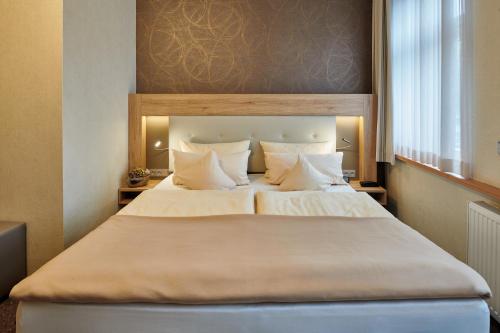 una camera da letto con un grande letto con lenzuola e cuscini bianchi di Ambient Hotel Zum Schwan a Gelsenkirchen