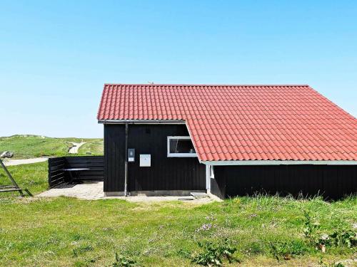 a black shack with a red roof in a field at 8 person holiday home in Harbo re in Vrist