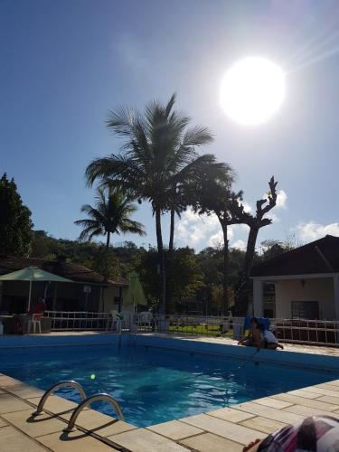 a swimming pool with palm trees and the sun at Chacara Estrela do Mar in Peruíbe