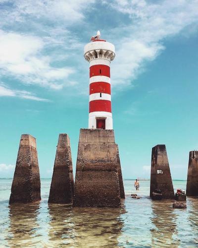 a red and white lighthouse sitting in the water at QUARTO/SALA COM VISTA P/ O MAR DE PAJUÇARA in Maceió