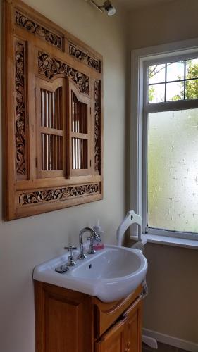 uma casa de banho com um lavatório branco e uma janela em Designer Cottage em Christchurch