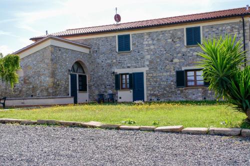 a stone house with a green lawn in front of it at Poggio Picchio in Bibbona