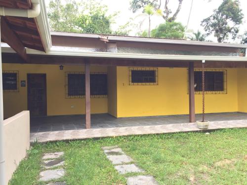 a yellow house with a porch and a yard at Casa em frente à praia Boracéia in Boracéia
