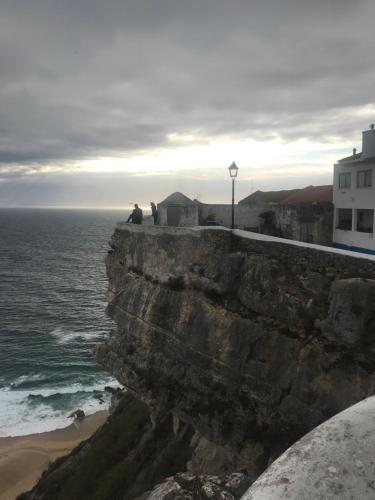 a man sitting on a cliff overlooking the ocean at O Melhor Sítio do Mundo - NOVO na Nazaré in Nazaré