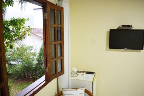 Habitación con ventana y TV en la pared. en Nova Suíte - centro de Domingos Martins + Café da manhã, en Domingos Martins