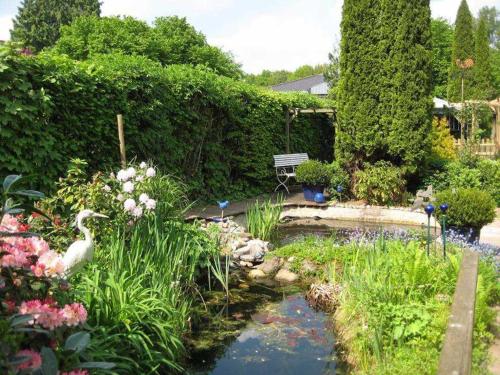 einen Garten mit einem Teich, Blumen und einer Bank in der Unterkunft Ferienwohnung Antonia, 15110 in Leer