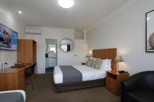 a hotel room with a large bed and a desk at Cadman Motor Inn and Apartments in Tamworth