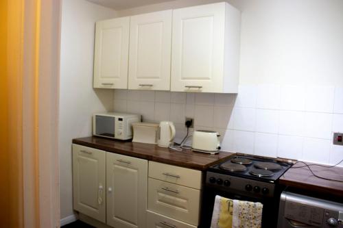a kitchen with white cabinets and a stove at Kempston Cosy Lodge in Bedford