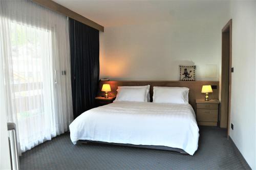 - une chambre avec un lit blanc et une grande fenêtre dans l'établissement Residenza e Appartamenti Le Colonnine, à Pozza di Fassa