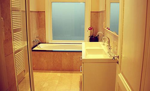 een badkamer met een bad, een wastafel en een raam bij Maison Indochine in Den Haag