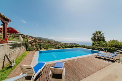 a villa with a swimming pool with chairs and the ocean at Villa Sol by Amazing Madeira in Ponta do Sol