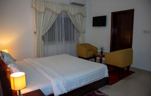 a bedroom with a bed and two chairs and a window at His Majesty's Hotel and Apartments in Accra