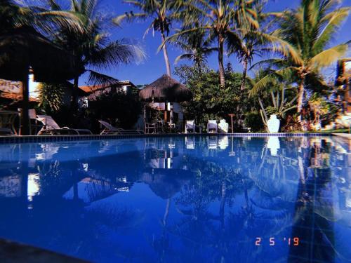 a swimming pool with palm trees and blue water at Hotel e Pousada La Dolce Vita in Canoa Quebrada