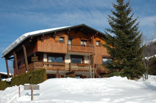 a large wooden building in the snow with a tree at Chalet La Licorne au pied des pistes in Notre-Dame-de-Bellecombe