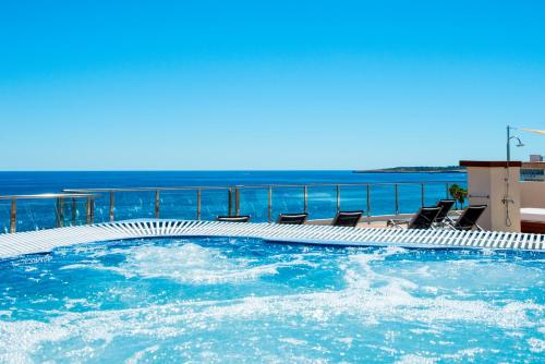 a swimming pool with chairs and the ocean in the background at Aparthotel Cap De Mar in Cala Bona