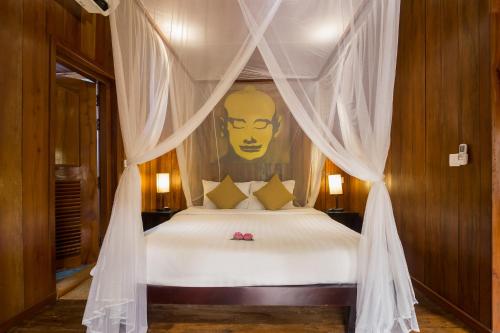 a bedroom with a canopy bed with a face on the wall at Wat Bo House in Siem Reap