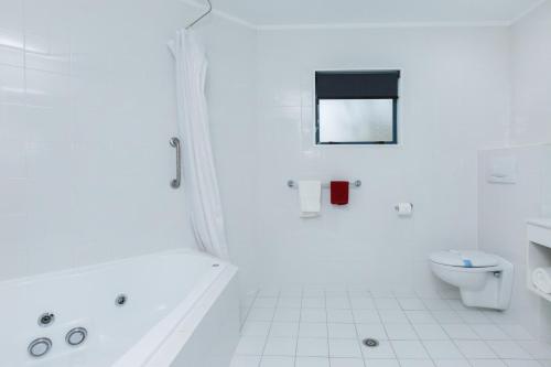 a white bathroom with a tub and a toilet at Aubyn Court Spa Motel in Palmerston North
