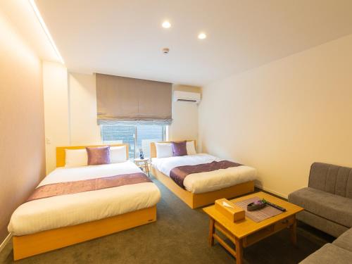 a hotel room with two beds and a couch at GRAND BASE Hiroshima Ekimae in Hiroshima