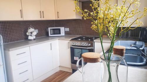 uma cozinha com armários brancos e um vaso com flores amarelas em Seymour Road - Birmingham BnBs em Oldbury