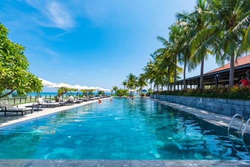 a swimming pool at a resort with palm trees and the ocean at Ocean Sunny Villas Da Nang in Danang