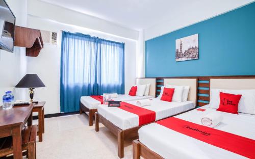 a room with two beds and a table and a desk at RedDoorz Plus near Rizal Junction in Puerto Princesa City
