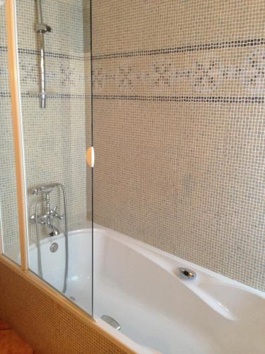 a bath tub with a shower and a glass door at Hospedería Ana Pilar in Porcuna