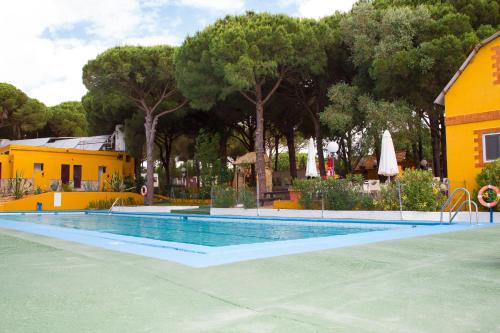 a swimming pool next to a yellow house and trees at Camping Vejer in Vejer de la Frontera