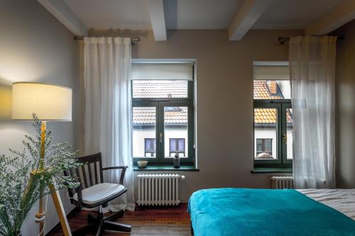 a bedroom with a bed and a chair and two windows at Apartamenty na Starówce / Old Town apartments in Toruń