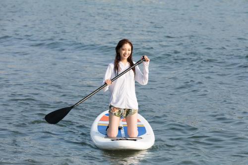 a girl is standing on a paddle board in the water at MARINE-Q in Inami