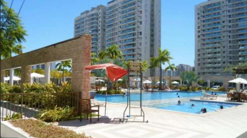 a swimming pool with a red umbrella and some buildings at Apartamento Parque Olímpico in Rio de Janeiro