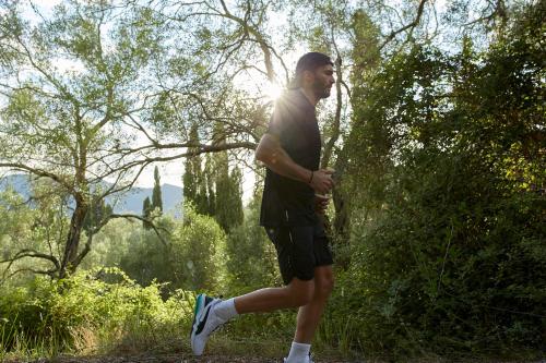 a man walking through a forest with the sun behind him at MarBella, Mar-Bella Collection in Agios Ioannis Peristeron