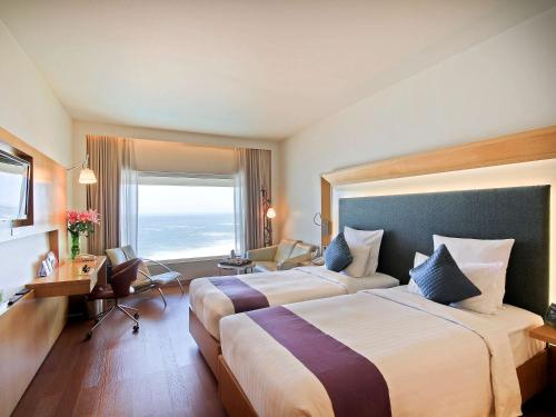 a hotel room with two beds and a desk at Novotel Visakhapatnam Varun Beach in Visakhapatnam