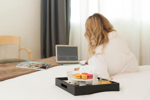 une femme assise sur un lit avec un plateau de nourriture dans l'établissement Nestos Hotel, à Xánthi