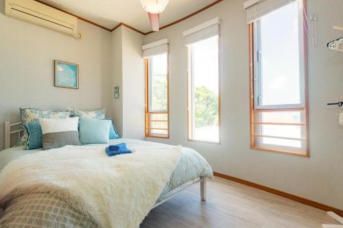 a bedroom with a bed and two windows at ペンション ラナカイハウス沖縄 in Onna