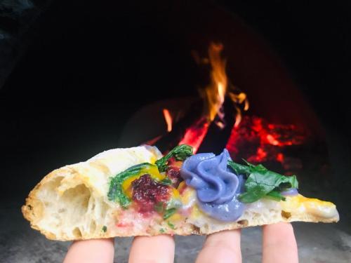 a person holding a slice of pizza with fire in the background at Borgo Rosso di Sera - Resort Country Chic in San Lucido