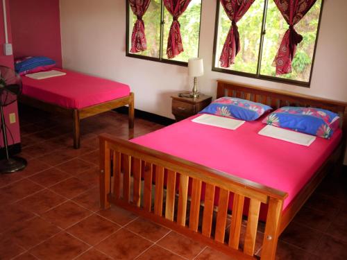 a room with two beds with pink sheets and windows at Hospedaje Soma in Moyogalpa