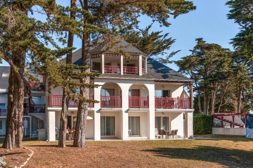 a large white house with red balconies and trees at Résidence Pierre & Vacances Premium Le Domaine de Cramphore in Le Pouliguen