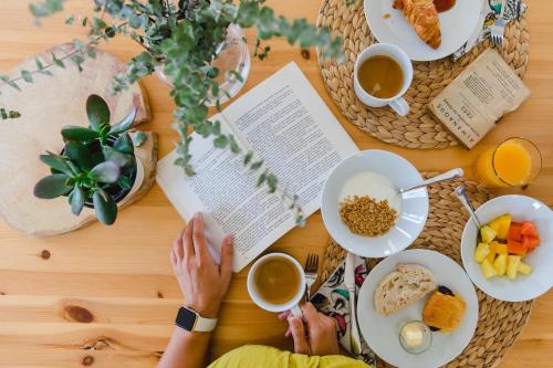 a woman sitting at a table reading a book and eating breakfast at CAMBEIROS - Guest House in Alenquer