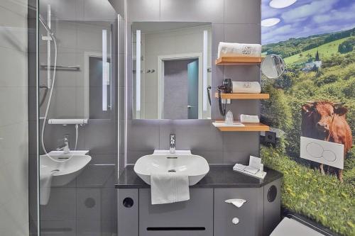 un baño con dos lavabos y una pintura de una vaca en Landhotel Naafs-Häuschen, en Lohmar