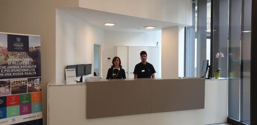 two people standing at a reception counter in an office at Hotel Cascina Fossata & Residence in Turin