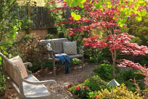 un jardín con 2 bancos, una mesa y flores en El Farolito B&B Inn, en Santa Fe