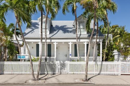a white fence in front of a white house with palm trees at Nyah - Adult Exclusive in Key West