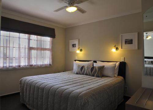 a bedroom with a bed with a ceiling fan and a window at Silver Fern Rotorua Suites & Spa in Rotorua
