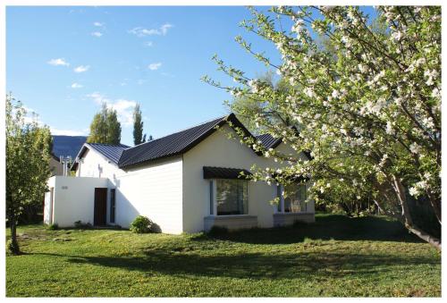 a white house with a flowering tree in the yard at El Puente Aparts- Departamentos Independientes in El Calafate