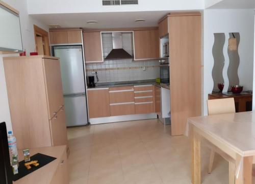 uma cozinha com armários de madeira, uma mesa e um frigorífico em APARTAMENTO EN SEGUNDA LINEA DE MAR, WIFI & A.C em Cubelles